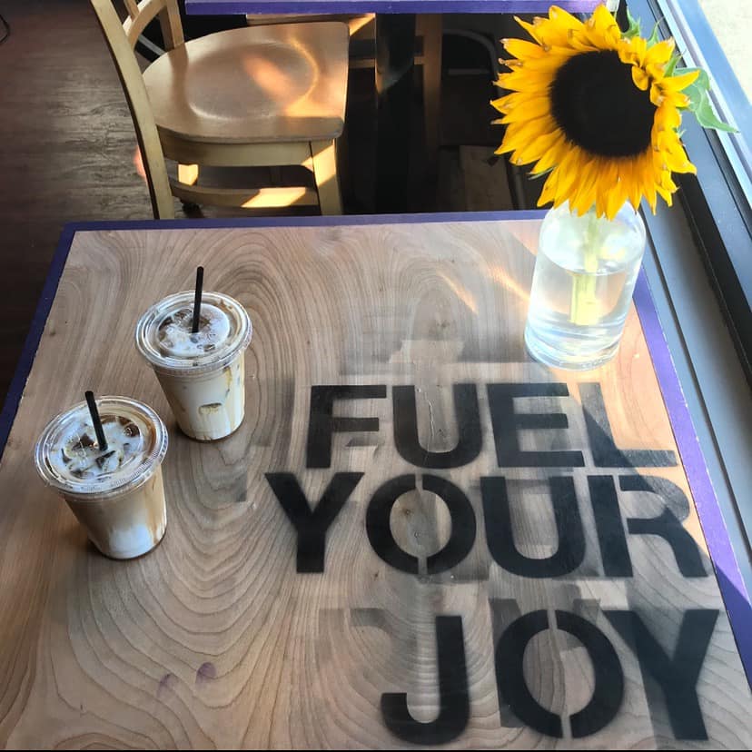 Two iced lattes are on a table that says "Fuel Your Joy"