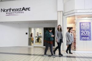 Three woman walking through a mall in front of a storefront with a sign that says Northeast Arc #opportunities