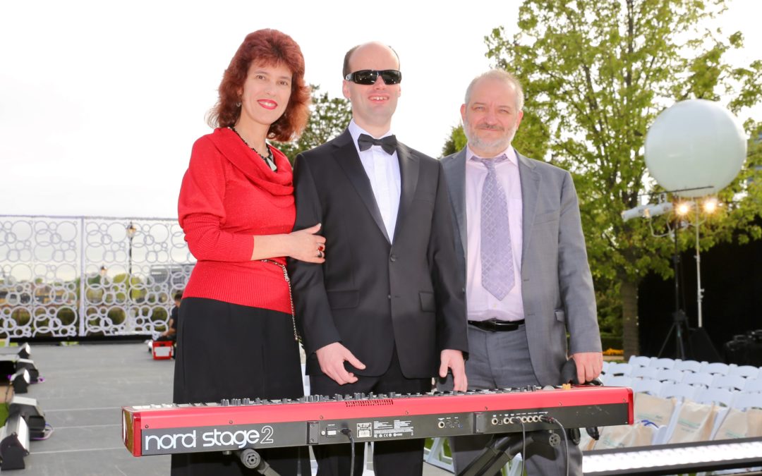 Santon is pictured with his parents. He is in a tuxedo standing in front of a keyboard and wearing black sunglasses. His mother Julia is to his left and wearing a red sweater. Santon's father, Aleksey, is on the right in a gray suit.