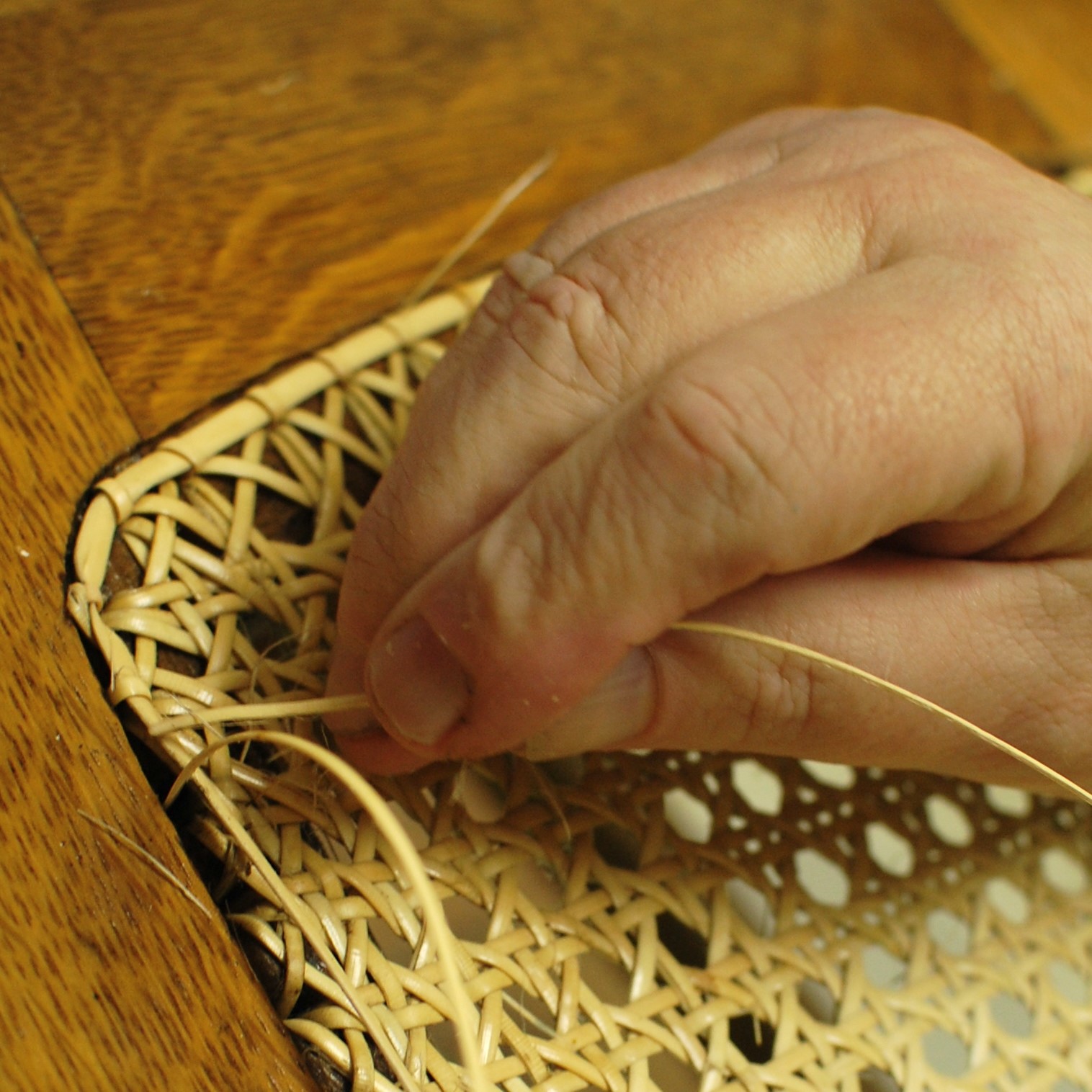 A close-up image of a hand caning a chair.