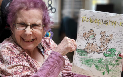 A smiling woman in a wheelchair holds up a drawing