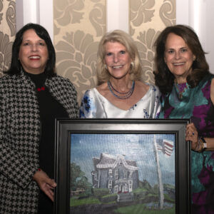 Lieutenant Governor Kim Driscoll, RoAnn Costin, and Jo Ann Simons. Costin is holding a painting of her home done by ArcWorks artist Polyvios Christoforos