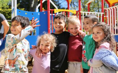 A smiling group of children stand in front of a playground structure