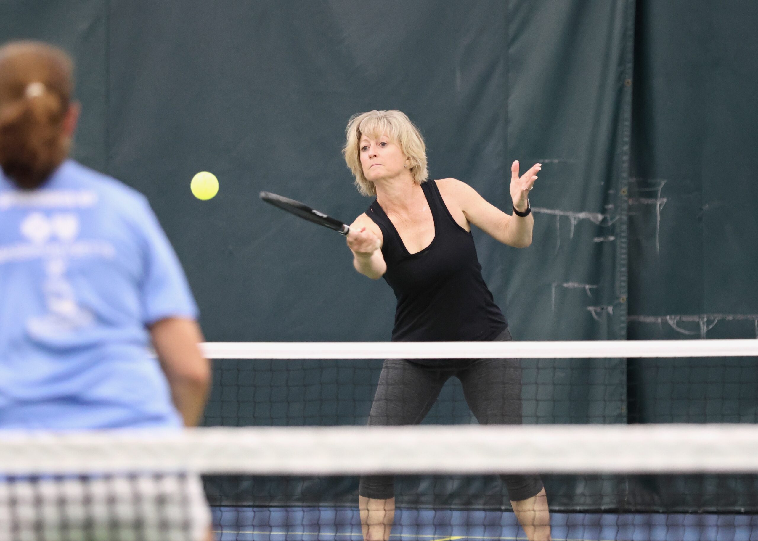 A woman in a black shirt hits the ball